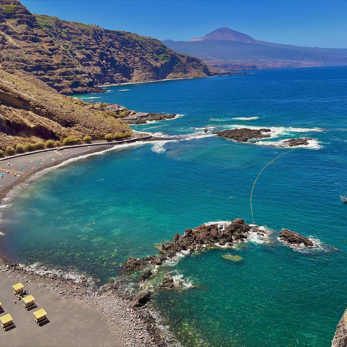 Vistas espectaculares de playa de arena negra volcánica, aguas turquesas cristalinas y majestuoso volcán al fondo. Paraíso costero con acantilados escarpados y bahía protegida ideal para relajarse.