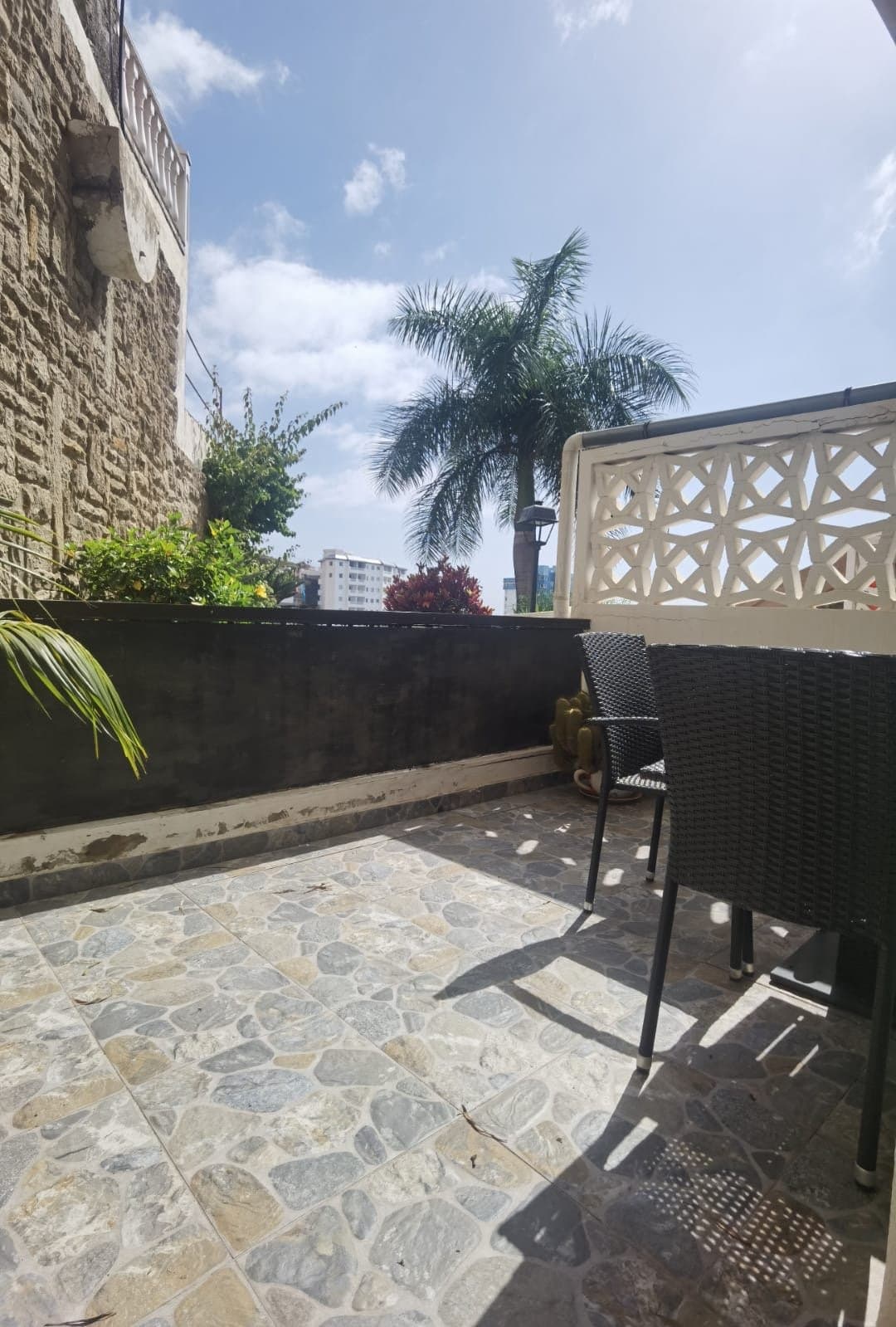 Terraza privada con vistas a la ciudad, equipada con cómoda zona de descanso. Perfecta para disfrutar del aire fresco y relajarse bajo el sol con palmeras tropicales.