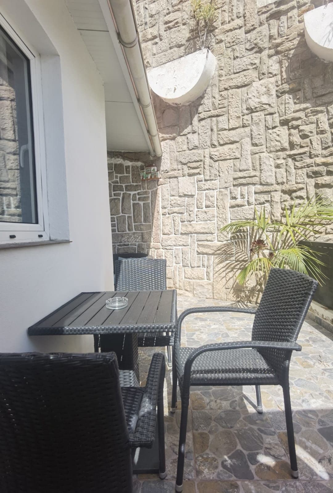 Acogedor porche privado con muebles de ratán, perfectamente sombreado por luminarias modernas. Ideal para relajarse y disfrutar del aire libre junto a la piedra natural de la fachada.